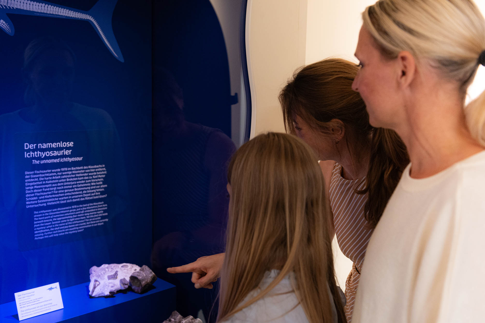 Familie steht vor einer Vitrine, darin werden Dinosaurier aus Österreich präsentiert: der Ichtyiosaurier